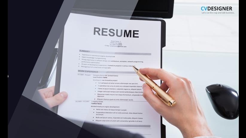 Person reviewing a printed resume with a pen in hand, next to a computer monitor.