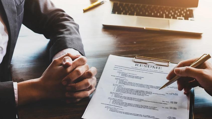 Job interview in progress with a resume on table and candidate clasping hands nervously.